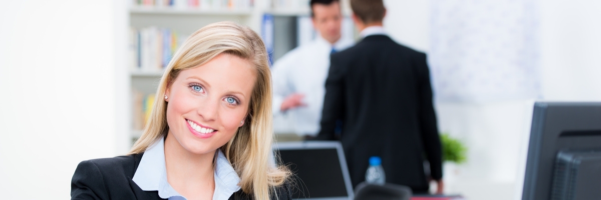 Eine junge Frau lächelt im Büro vor dem Computer